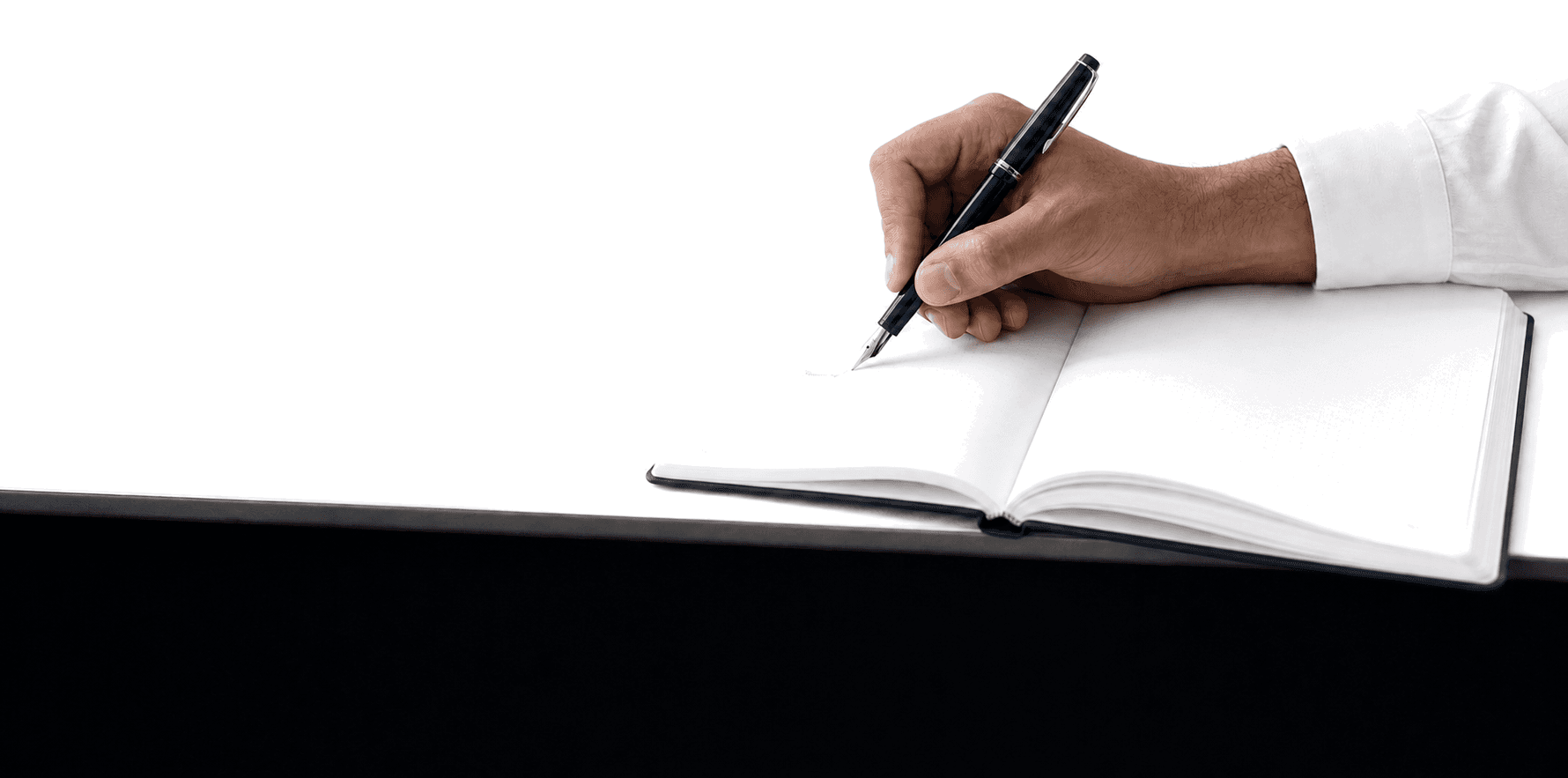 Mão adulta escreve com uma caneta azul em um caderno aberto sobre uma mesa branca.